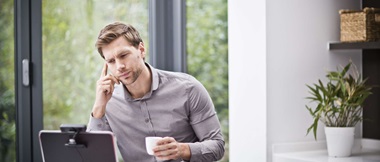 Dans cette scène de travail à distance hybride, un homme est assis à son bureau à domicile et son ordinateur portable est équipé d'une webcam. 
