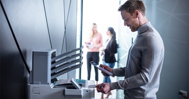 Group of people in a modern office, with one person using a multifunction printer
